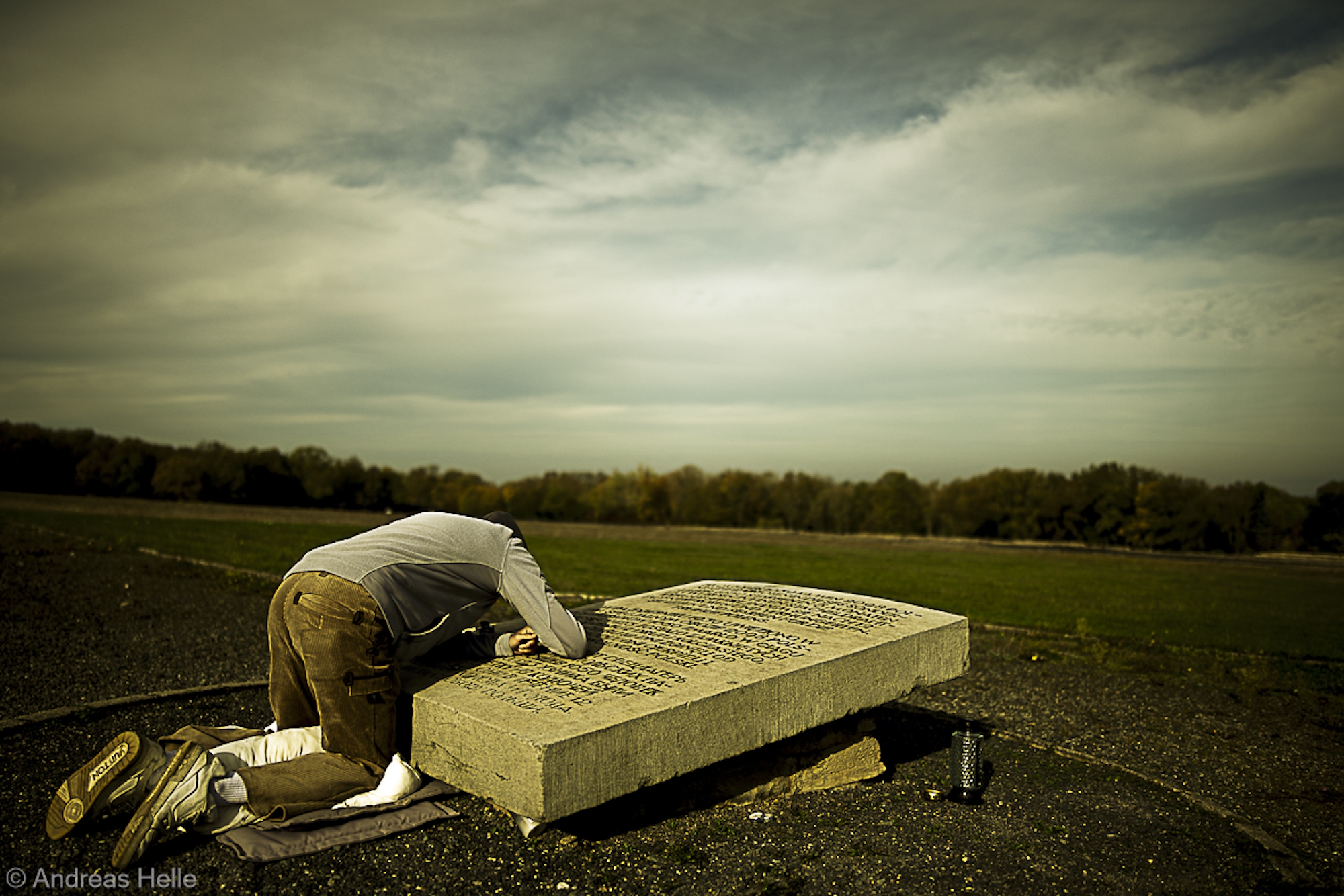 Eine Person kniet und beugt sich über eine große beschriftete Steinplatte, die in einem offenen Außenbereich auf dem Boden liegt. (KI generierte Beschreibung)