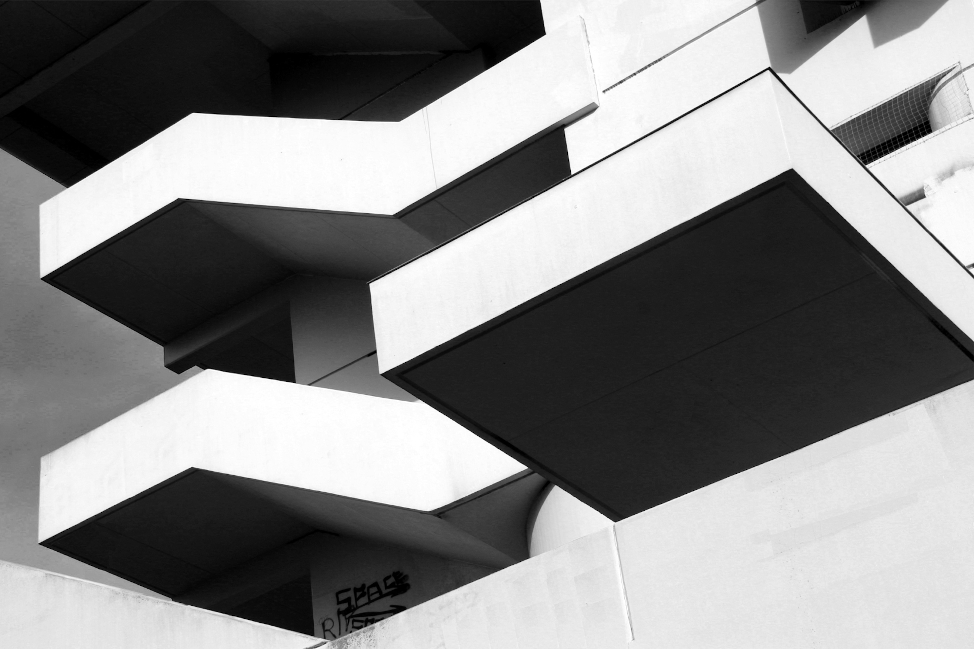 Schwarz-Weiß-Foto eines modernen Gebäudes mit mehreren kantigen, vorspringenden Balkonen und scharfen architektonischen Linien. (KI generierte Beschreibung)