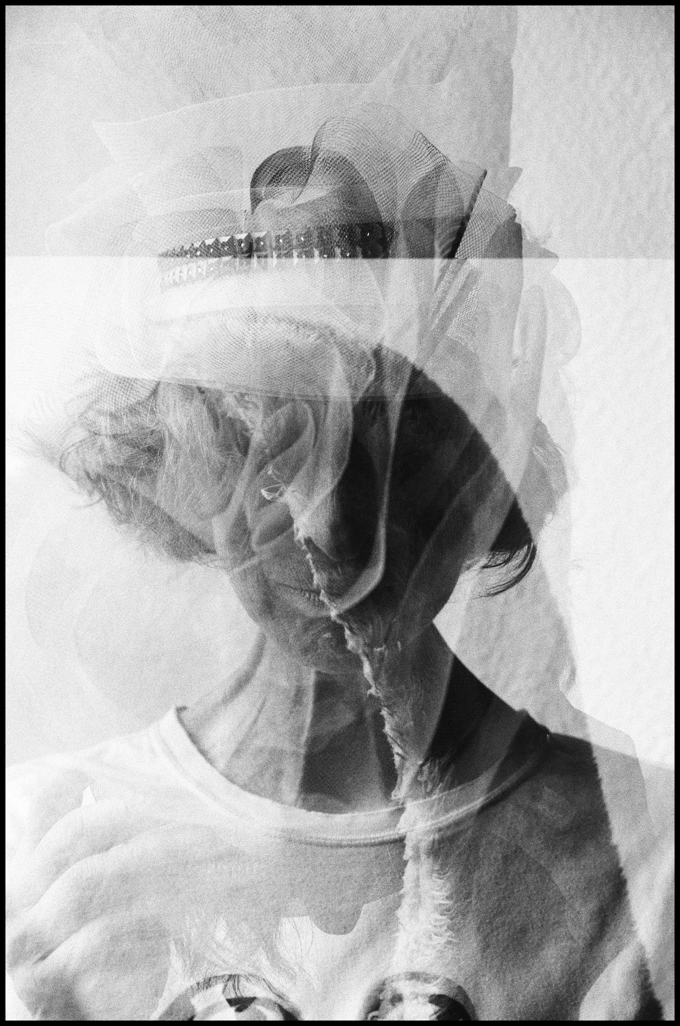 Schwarz-Weiß-Doppelbelichtungsfoto, das eine Person mit Hut zeigt, deren Gesicht durch überlagerte Bilder von Blumen und Strukturen teilweise verdeckt wird. (KI generierte Beschreibung)