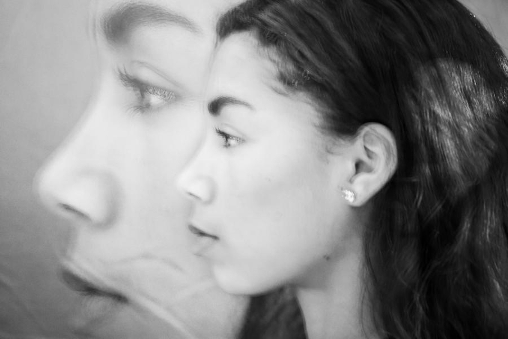 Ein Schwarz-Weiß-Foto zeigt das Profil einer Frau, überlagert von einem größeren, halbtransparenten Profil ihres Gesichts im Hintergrund. (KI generierte Beschreibung)